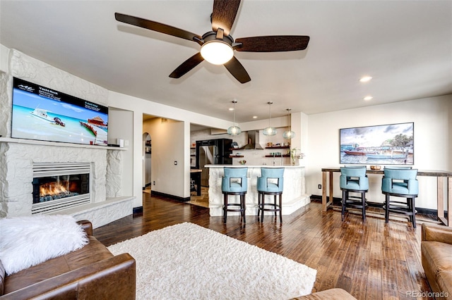 living room with a stone fireplace and dark wood-type flooring