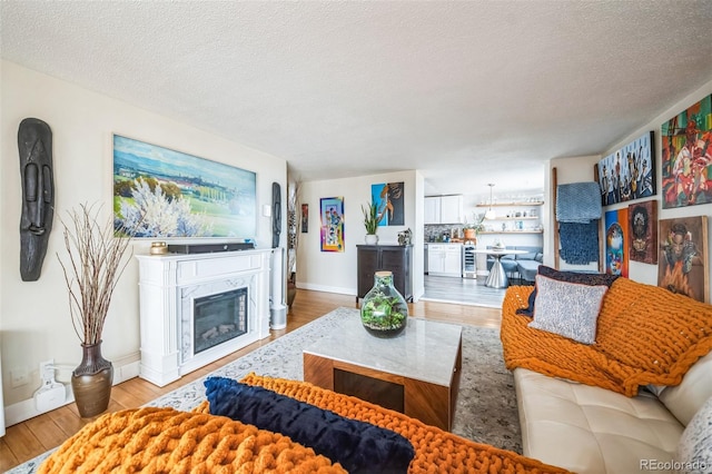 living area featuring baseboards, a fireplace, a textured ceiling, and light wood-style floors