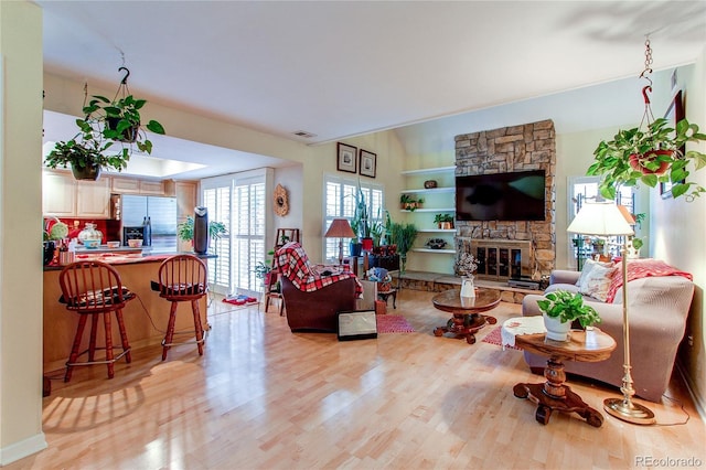 living room with built in features, a fireplace, and light hardwood / wood-style flooring