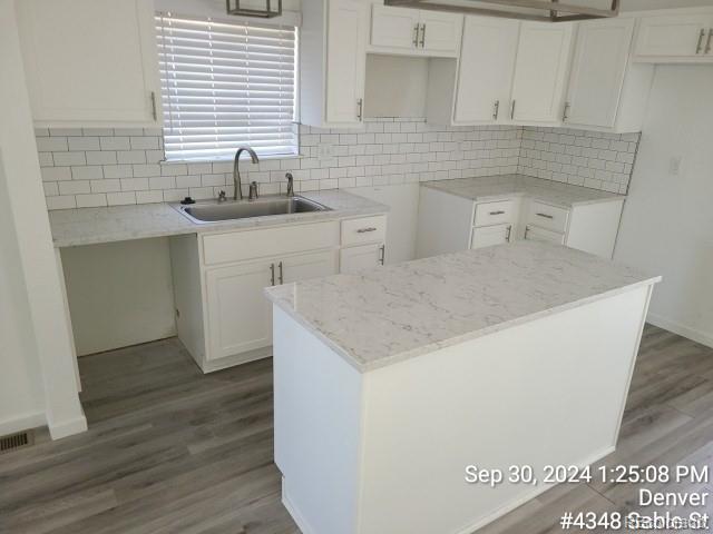 kitchen featuring hardwood / wood-style flooring, sink, white cabinets, a kitchen island, and backsplash