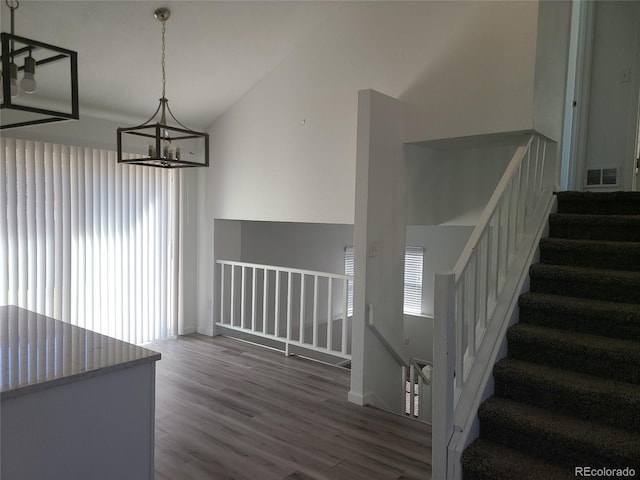 staircase featuring an inviting chandelier, lofted ceiling, and hardwood / wood-style floors