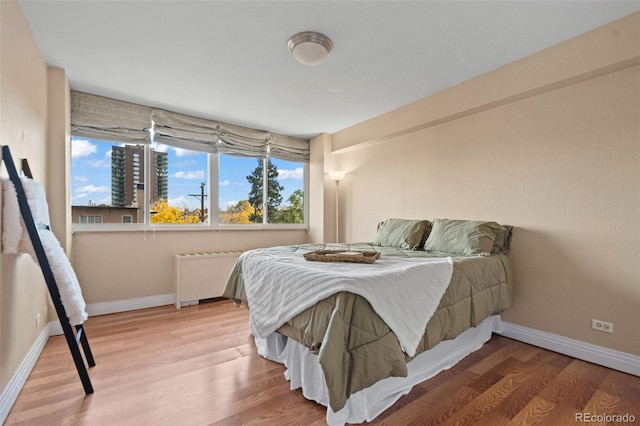 bedroom featuring hardwood / wood-style floors, radiator heating unit, and multiple windows