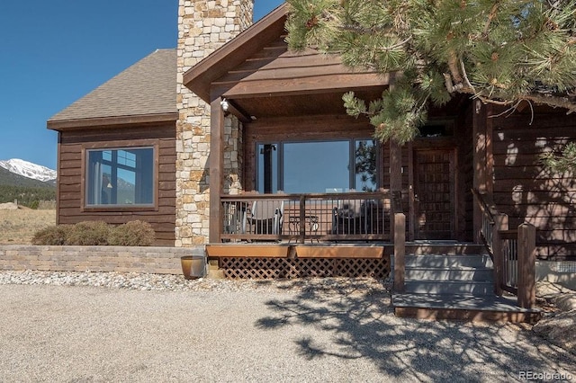 doorway to property featuring covered porch, stone siding, a chimney, and roof with shingles