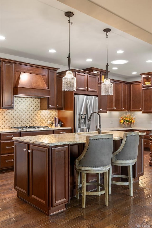 kitchen featuring hanging light fixtures, appliances with stainless steel finishes, a center island with sink, and custom exhaust hood