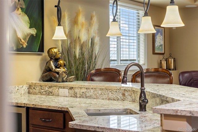 interior details featuring decorative light fixtures, sink, light stone counters, and beverage cooler