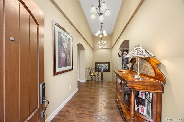 foyer entrance featuring arched walkways, a chandelier, dark wood-style flooring, and baseboards
