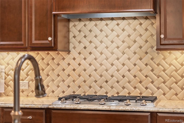 kitchen view of backsplash, stainless steel gas stovetop, and light stone countertops