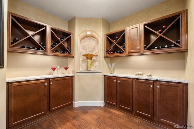 indoor dry bar featuring dark wood-type flooring and baseboards