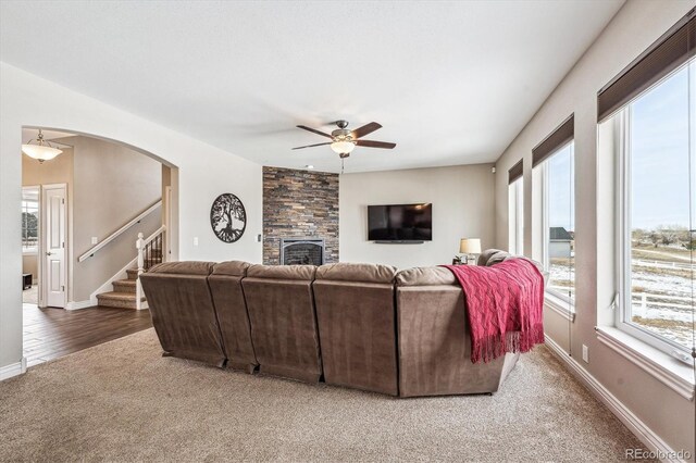 living room with arched walkways, a fireplace, ceiling fan, baseboards, and stairs