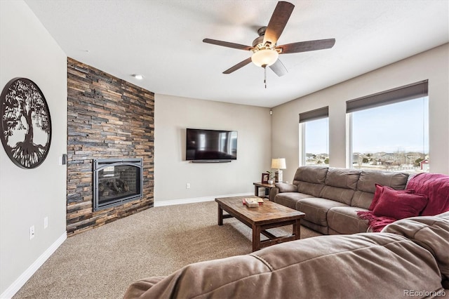 carpeted living area with ceiling fan, a stone fireplace, and baseboards