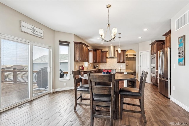 dining space featuring baseboards, arched walkways, wood finished floors, an inviting chandelier, and recessed lighting