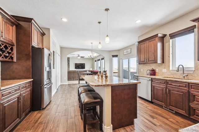 kitchen featuring open floor plan, a center island, light stone countertops, stainless steel appliances, and a sink