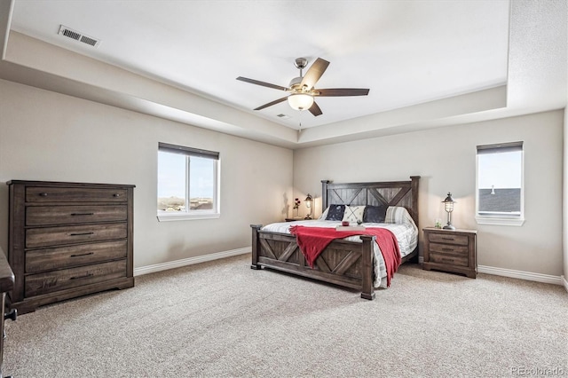 bedroom featuring baseboards, multiple windows, visible vents, and a tray ceiling