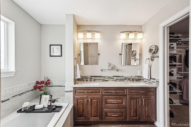 full bathroom with a spacious closet, double vanity, a jetted tub, and a sink