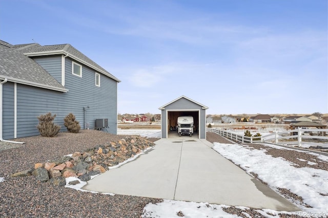 view of snowy exterior with an outbuilding, cooling unit, a garage, fence, and driveway