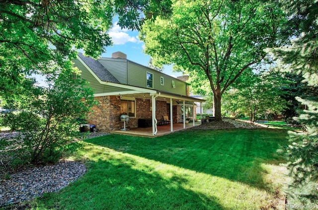 back of house with brick siding, a patio, a chimney, and a lawn