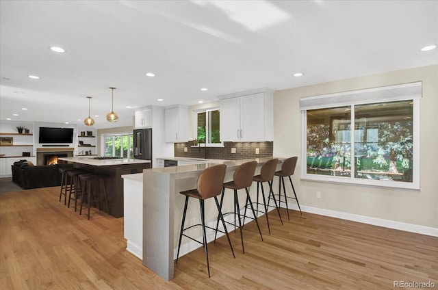 kitchen with high end refrigerator, white cabinetry, light wood-style floors, open floor plan, and a kitchen breakfast bar