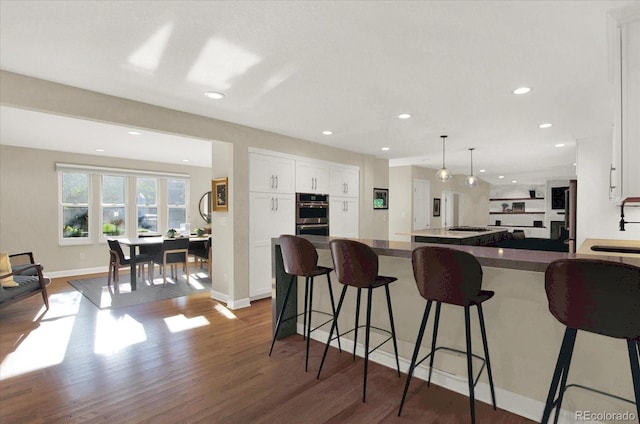 kitchen with stainless steel double oven, a breakfast bar, white cabinetry, open floor plan, and dark wood finished floors