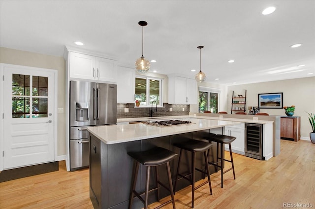 kitchen with light wood finished floors, appliances with stainless steel finishes, white cabinets, beverage cooler, and a peninsula