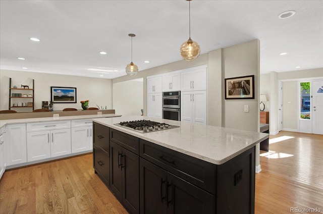 kitchen with stainless steel appliances, white cabinetry, a kitchen island, and light wood-style flooring