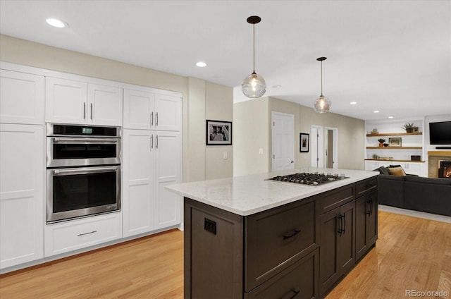 kitchen featuring appliances with stainless steel finishes, open floor plan, decorative light fixtures, light wood-style floors, and white cabinetry