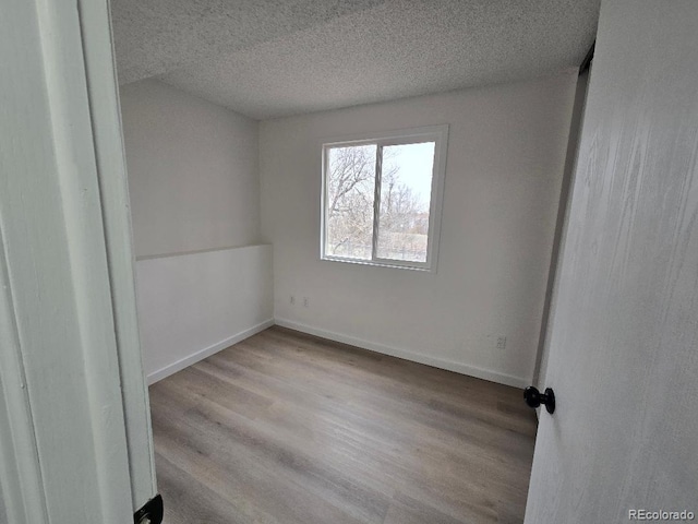 unfurnished room with a textured ceiling, baseboards, and wood finished floors