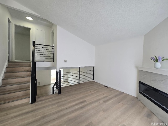 living room featuring a textured ceiling, a glass covered fireplace, wood finished floors, baseboards, and stairs