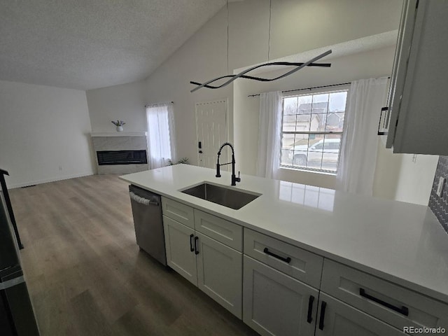 kitchen with a sink, a textured ceiling, dark wood finished floors, dishwasher, and vaulted ceiling