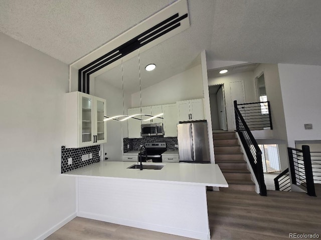 kitchen with glass insert cabinets, appliances with stainless steel finishes, a peninsula, wood finished floors, and a sink