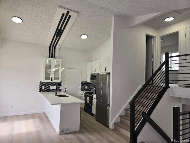 kitchen featuring glass insert cabinets, light wood-type flooring, a peninsula, stainless steel appliances, and a sink