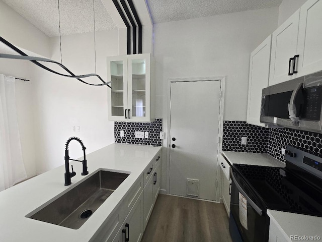 kitchen with a sink, stainless steel microwave, range with electric stovetop, white cabinets, and decorative backsplash