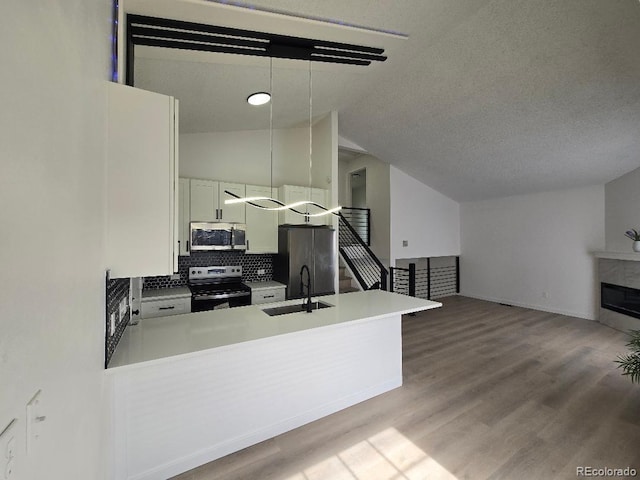 kitchen with wood finished floors, a peninsula, a sink, stainless steel appliances, and tasteful backsplash