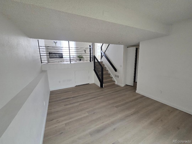 below grade area featuring stairs, wood finished floors, baseboards, and a textured ceiling