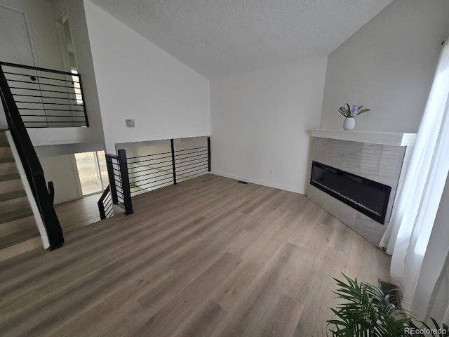 living room featuring a tiled fireplace, a textured ceiling, lofted ceiling, and wood finished floors