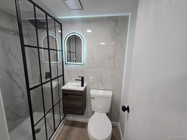 bathroom featuring a shower stall, wood finished floors, toilet, vanity, and tile walls