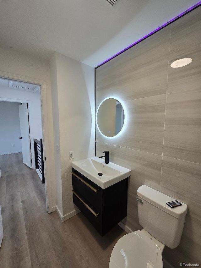 half bath with wood finished floors, vanity, tile walls, baseboards, and toilet