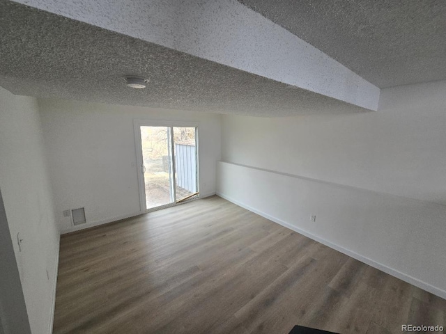 spare room featuring baseboards, visible vents, wood finished floors, and a textured ceiling