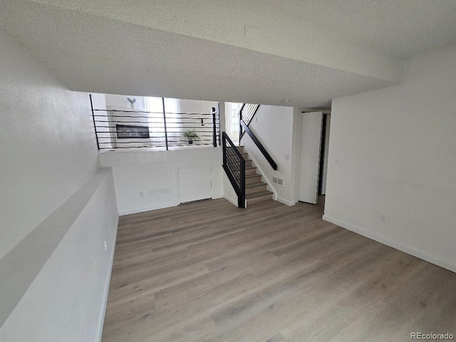 basement featuring baseboards, wood finished floors, a textured ceiling, and stairs