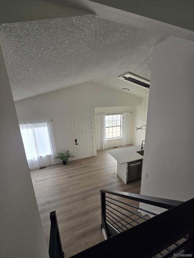 additional living space with vaulted ceiling, wood finished floors, a sink, and a textured ceiling