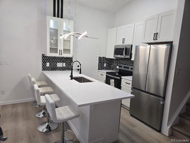 kitchen featuring a kitchen breakfast bar, a sink, decorative backsplash, wood finished floors, and appliances with stainless steel finishes