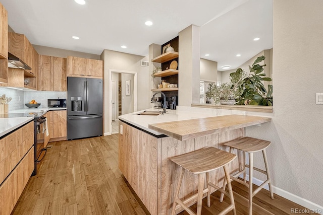 kitchen featuring backsplash, a kitchen breakfast bar, sink, light wood-type flooring, and stainless steel appliances