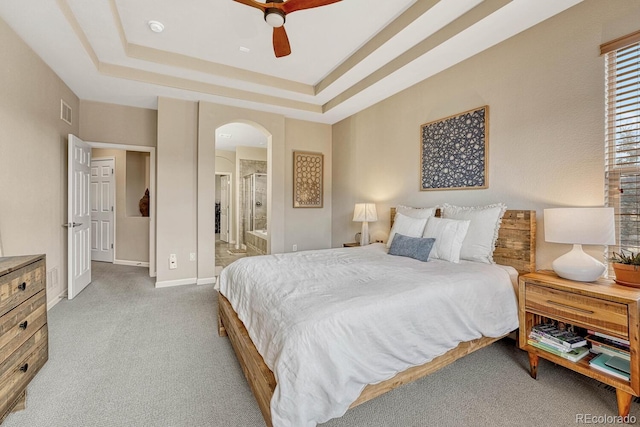 carpeted bedroom featuring ensuite bathroom, ceiling fan, and a tray ceiling