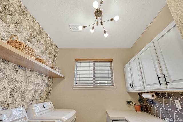 laundry room featuring a notable chandelier, washer and dryer, cabinets, and a textured ceiling