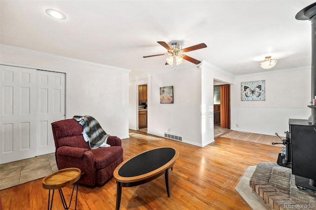 living room featuring a wood stove, crown molding, ceiling fan, and light hardwood / wood-style floors