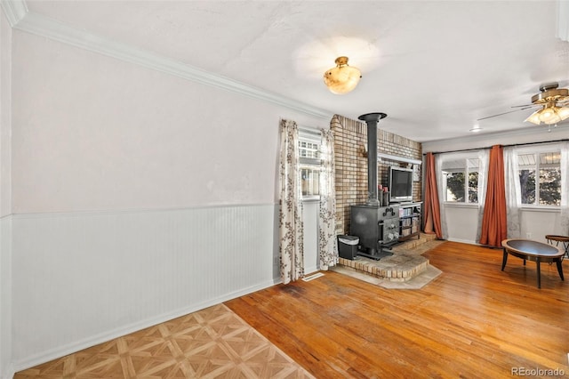 unfurnished living room with ceiling fan, a wood stove, and ornamental molding