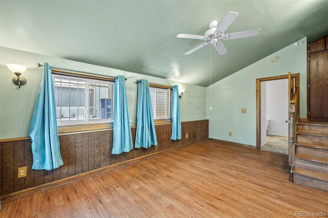 spare room featuring ceiling fan, light wood-type flooring, wooden walls, and vaulted ceiling