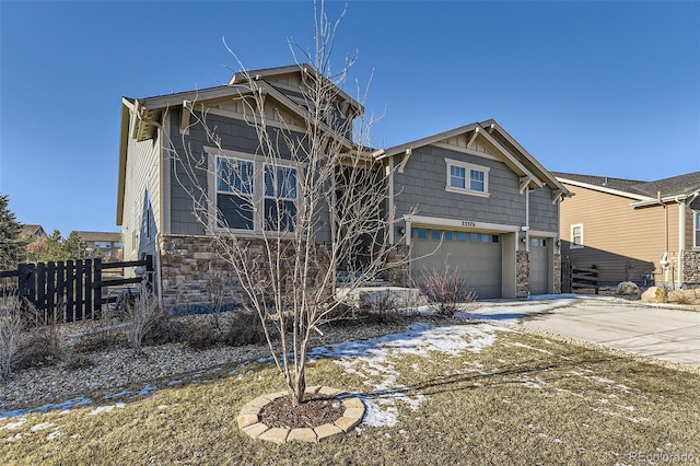 rear view of property with driveway, stone siding, a garage, and fence