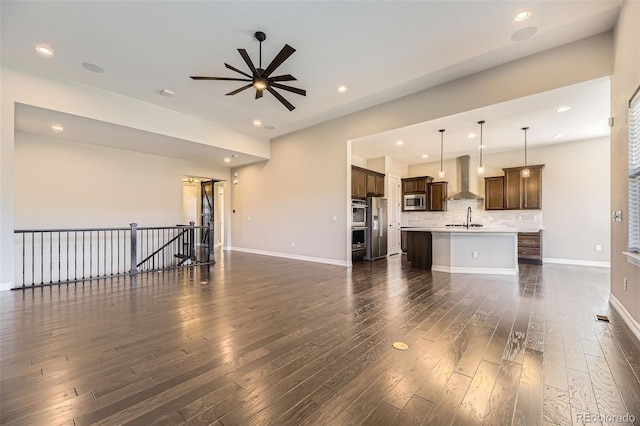 unfurnished living room featuring dark wood-type flooring, recessed lighting, a sink, and baseboards