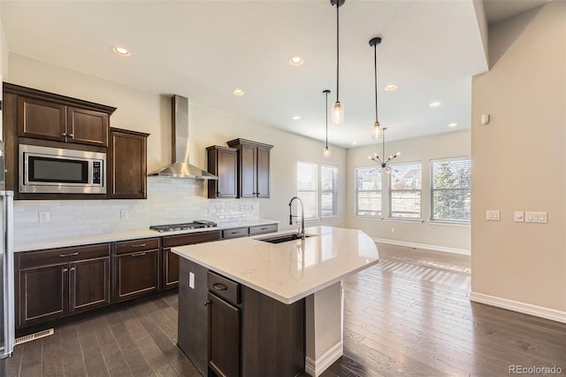 kitchen with a center island with sink, decorative backsplash, wall chimney exhaust hood, stainless steel appliances, and a sink