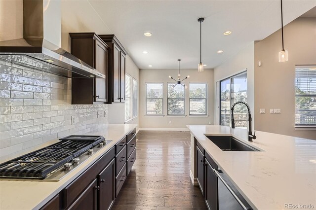 kitchen with stainless steel appliances, dark wood-type flooring, a sink, dark brown cabinets, and wall chimney exhaust hood